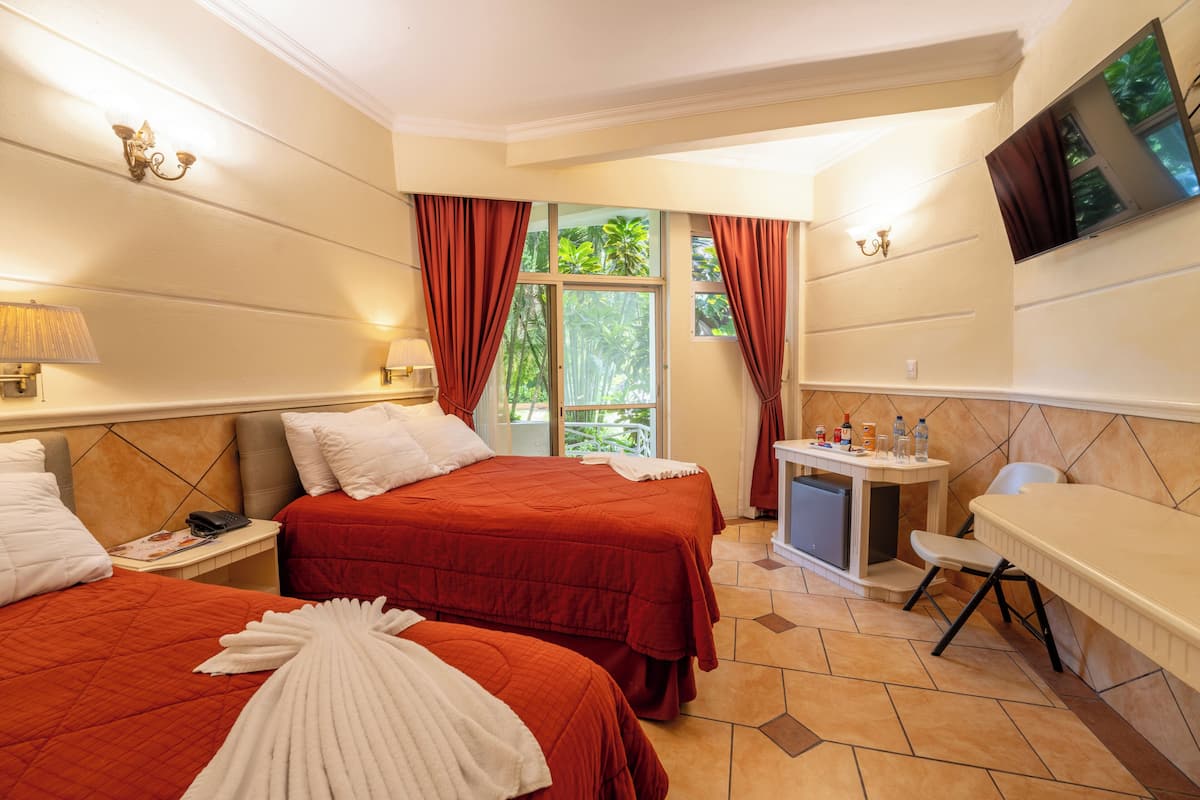 Habitación de hotel con dos camas, un escritorio pequeño, un televisor y una ventana con cortinas.