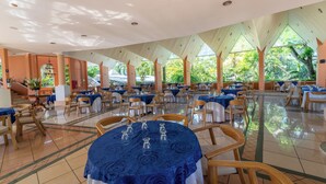 Un amplio comedor interior con mesas redondas, sillas y una lámpara colgante central.