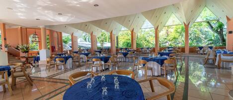 A spacious indoor dining area with round tables, chairs, and a central chandelier.