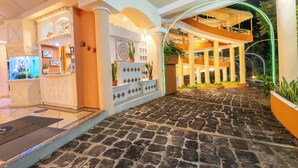 Un vestíbulo de hotel con piso de adoquines, un mostrador de recepción y una escalera que conduce a un nivel superior.