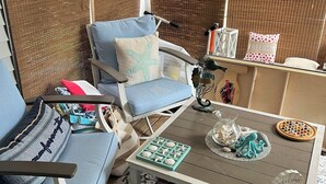 A beach-themed room with a blue chair, a small table with decorative items, and a wicker chair. - Charming Cottage for Rent at Beach Dreams Cottages, Wells, Maine! Unit #229 (Wells)