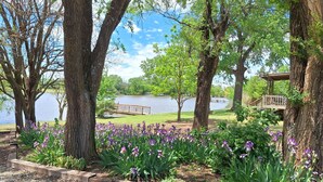 A serene park with a lake, trees, and purple flowers. - Kansas Lake House With Private Boat Dock (Anthony)