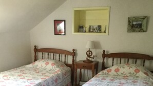 Ein Schlafzimmer mit zwei Einzelbetten, einem kleinen Nachttisch mit Lampe, einem Spiegel und einem Regal mit Dekoration.