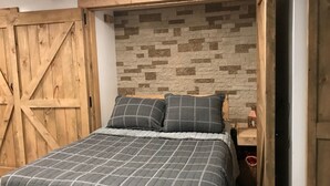 A bedroom with a bed, wooden headboard, and a stone-patterned wall. - Cozy Condo (Cass)