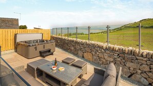 An outdoor patio with a hot tub, seating, and a stone wall. - 3 bedroom accommodation in Llandanwg (Llandanwg)