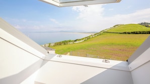 A view from a window overlooking a grassy landscape with a body of water and distant mountains. - 3 bedroom accommodation in Llandanwg (Llandanwg)