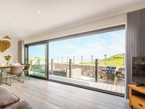 A modern room with a large sliding glass door leading to a balcony with a stone wall and a view of the sea.