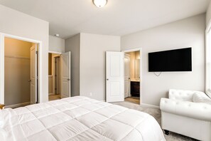 Ein Schlafzimmer mit einem großen Bett, einem weißen Sessel, einem flachbildfernseher an der Wand und mehreren Türen zu anderen Räumen.