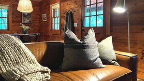 Et hyggeligt rum med en lædersofa, en hængende lampe og et stort vindue med udsigt til grøn vegetation.