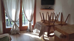 Une pièce avec une table en bois, un téléviseur accroché au mur et une fenêtre avec des rideaux.