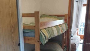 Une chambre avec un lit superposé, dont les structures sont en bois et la literie est à rayures.