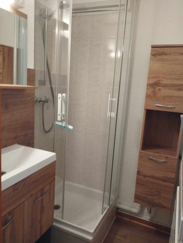 Un baño con ducha envuelta en vidrio, tocador de madera y espejo.