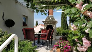 Une terrasse avec une table et des chaises, un four en briques et des plantes en pot.