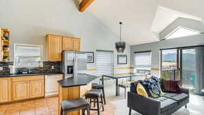 A modern kitchen with wooden cabinets, a central island with stools, a refrigerator, and a dining area with a glass table and chairs. - 6 Mi to Skiing: Mtn-View Fraser Duplex (Fraser)