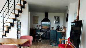Una cocina moderna con una isla central, una zona de comedor con una mesa de madera y sillas rosas, y una escalera con barandillas negras.