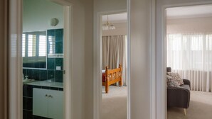 A hallway leading to a bedroom with a bed, a bathroom with a mirror and sink, and a living area with a sofa and curtains. - Yamacilla House: Spectacular Views in Blackheath! (Blackheath)