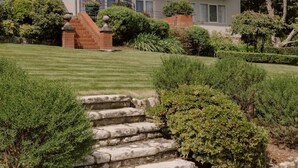 A two-story building with a flat roof, a brick entrance, and a well-maintained lawn with stone steps leading to the entrance. - Yamacilla House: Spectacular Views in Blackheath! (Blackheath)
