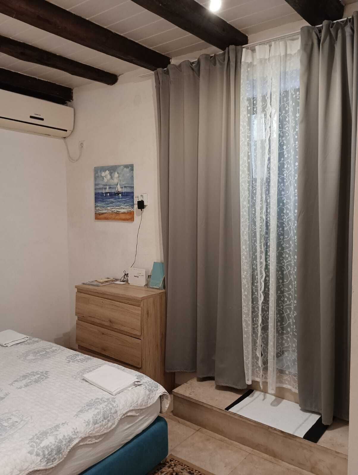 Ein Schlafzimmer mit einem Bett, einer hölzernen Kommode, einem Bild an der Wand und einem Fenster mit Vorhängen.