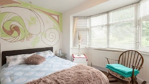 Un dormitorio con cama, una mecedora, una ventana con persianas y un mural en la pared.
