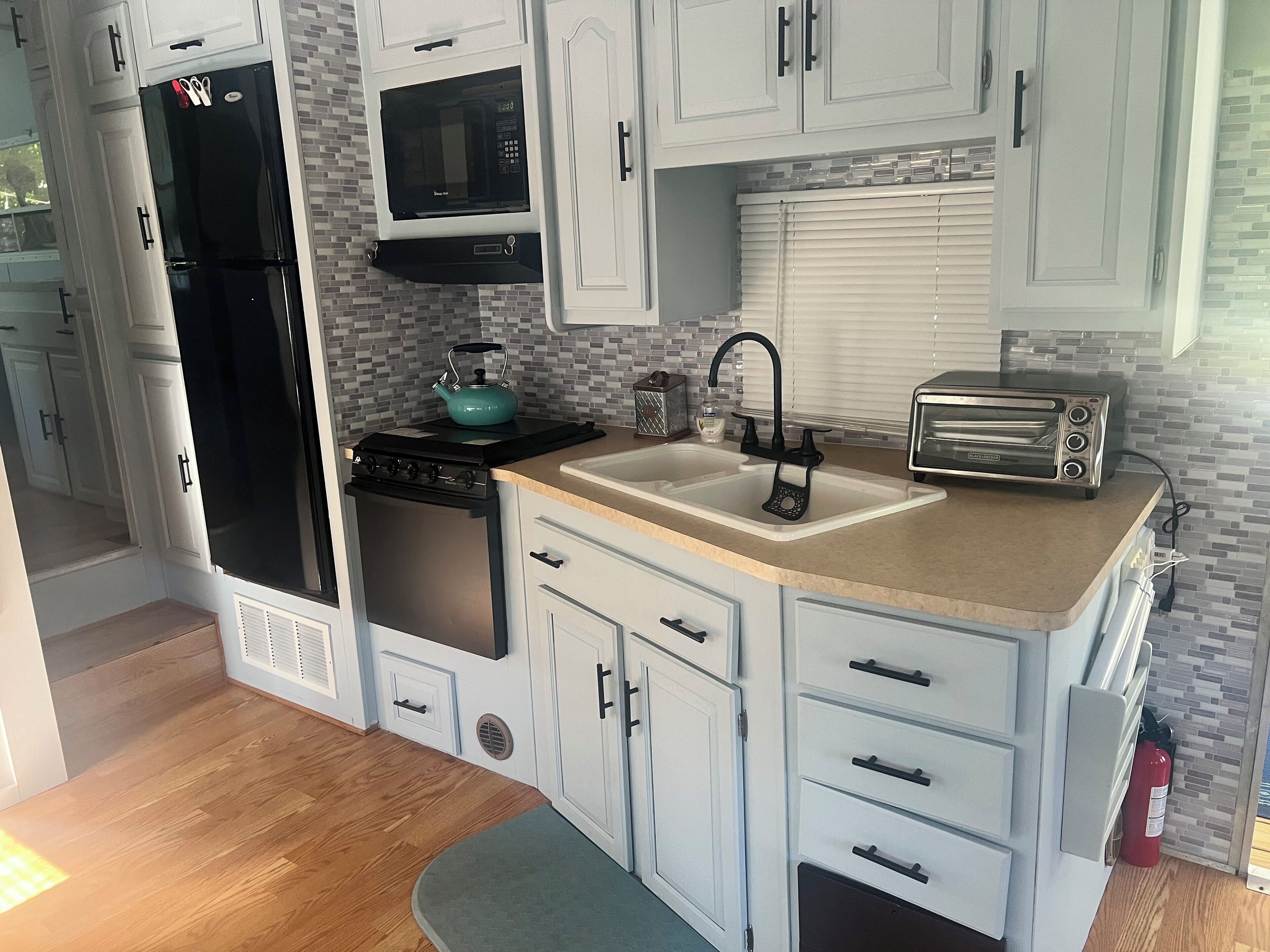A compact kitchen with a refrigerator, microwave, stove, sink, and toaster.
