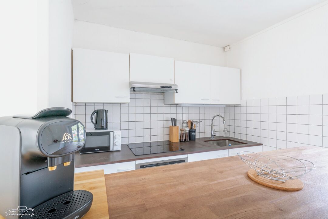 A modern kitchen with white cabinets, a black coffee machine, a sink, and a wooden countertop.
