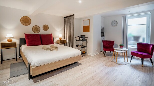 A modern hotel room with a large bed, two red chairs, a small table, and a window with curtains. - Casafamilia - Nantes Bord de Loire (Rezé)