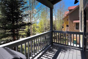 A wooden deck with a railing, overlooking a forested area and a building with a red roof. - Horseshoe Haven, Immaculate 2BD/2BA, Pet friendly! (Mt. Crested Butte)