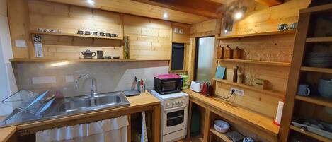 A compact kitchen with wooden walls, a stainless steel sink, a microwave, and a small oven.
