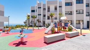 Un parque infantil con juegos de colores y un edificio al fondo.