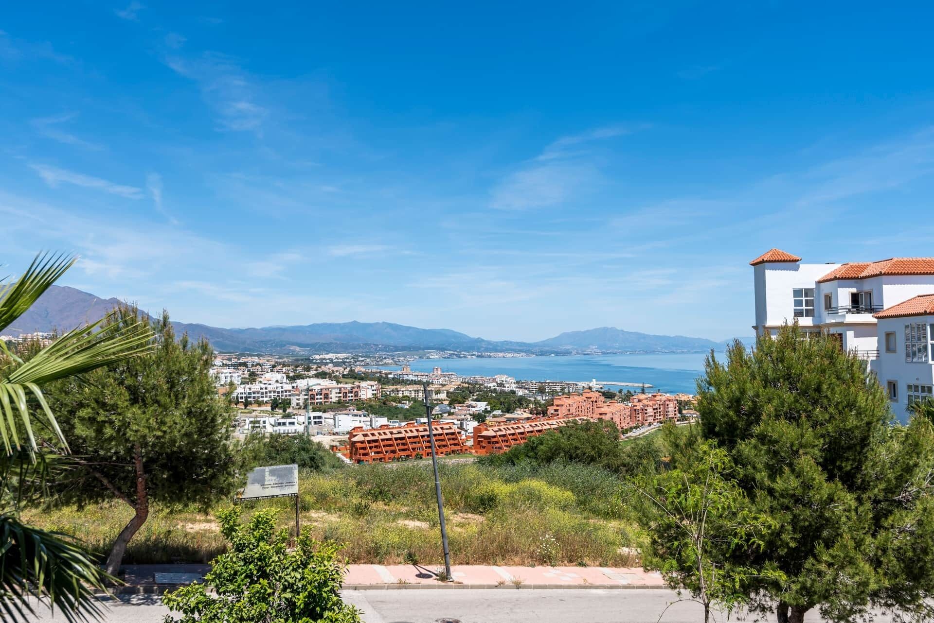 A coastal cityscape with a view of the sea and mountains in the distance.