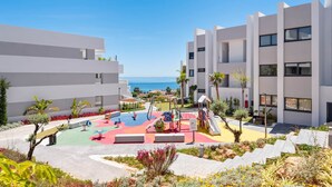 Un edificio moderno con un área de juegos que incluye estructuras coloridas y palmeras.