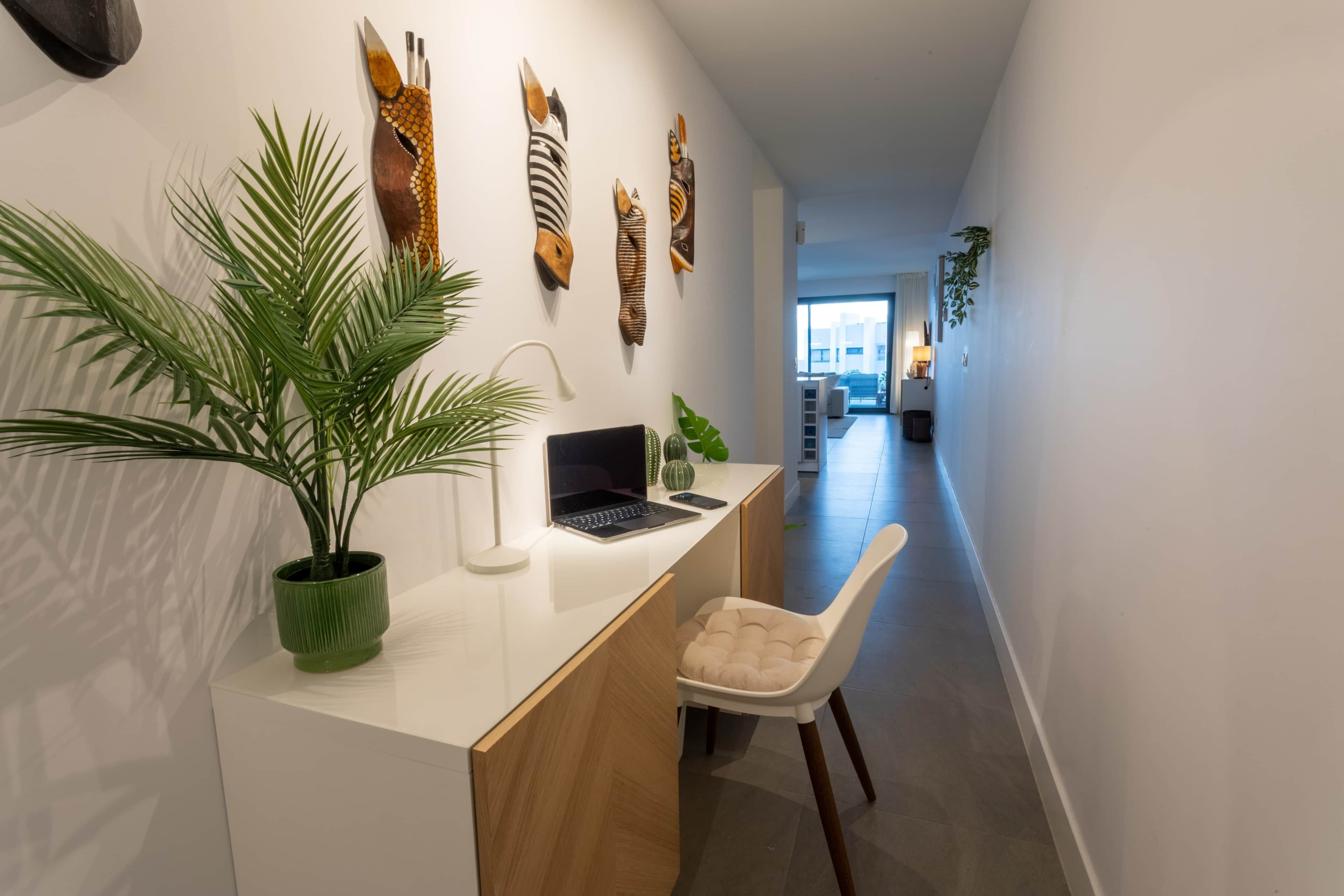 A modern kitchen with a white countertop, a laptop, a green plant, and a white chair.