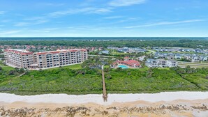 Vue aérienne d’une station balnéaire comprenant plusieurs bâtiments, une plage et une jetée.