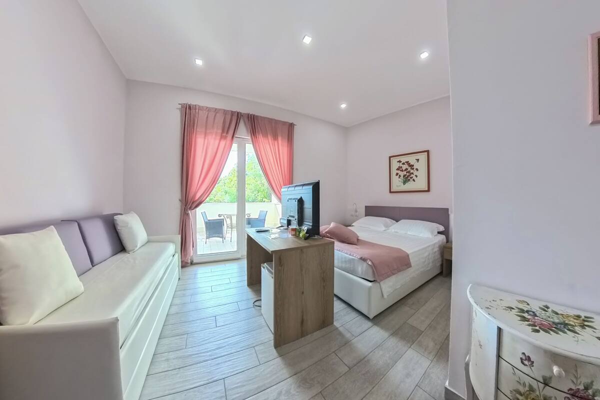A room with a sofa, a bed, a desk with a computer, and a window with curtains.