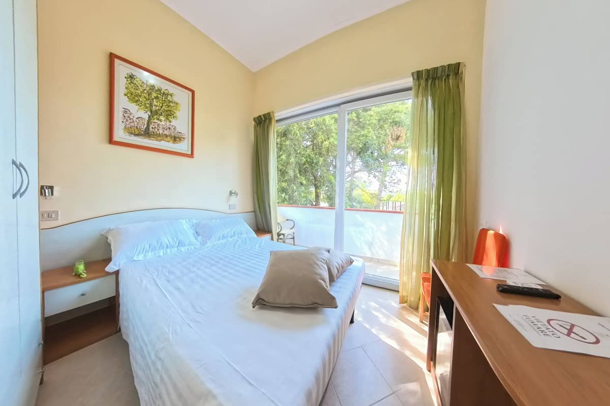 A bedroom with a bed, a nightstand, a desk, a framed picture, and a window with curtains.
