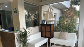A reception area with a counter, a seating area with a sofa and a table, a potted plant, and a cabinet.