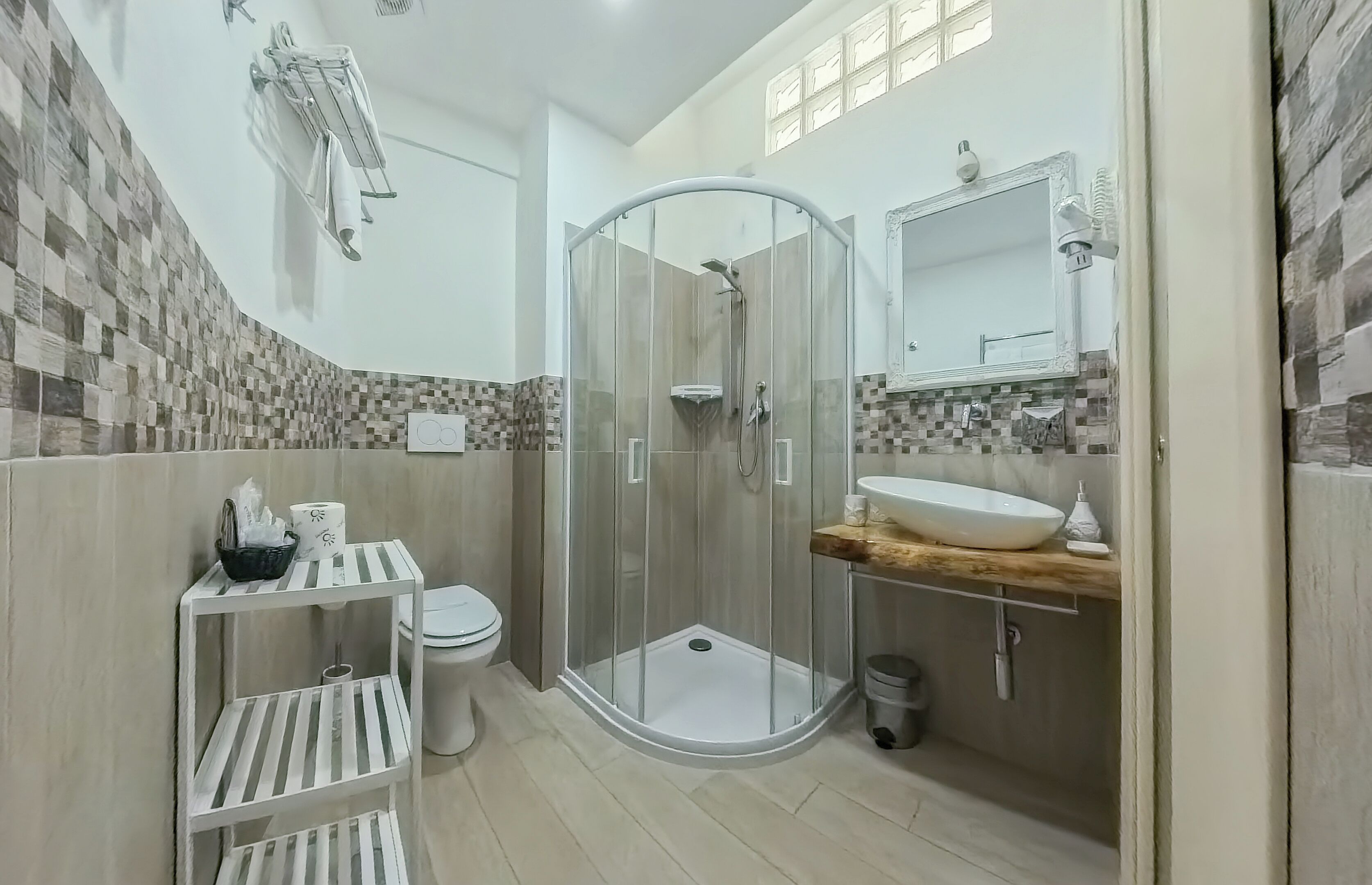 A modern bathroom with a glass-enclosed shower, a white toilet, a sink with a wooden countertop, and a tiled backsplash.
