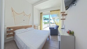 A hotel room with a bed, a desk with a TV, a chair, and a balcony with curtains.