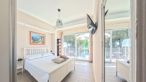 A bedroom with a bed, a painting, a TV, and a balcony with outdoor furniture.