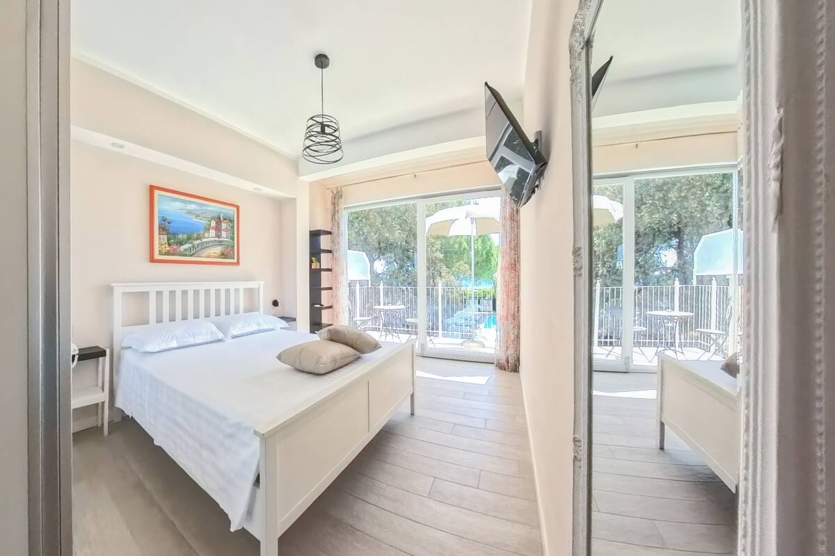 A bedroom with a bed, a painting, a TV, and a balcony with outdoor furniture.