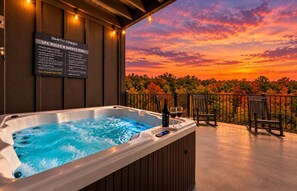 Un jacuzzi sur un balcon avec vue sur le coucher de soleil, un panneau indiquant les règles du spa et deux chaises.