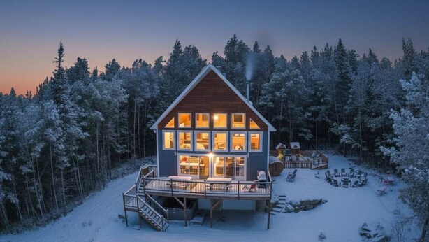 Eine Holzblockhütte mit einer Veranda, umgeben von einem verschneiten Wald.