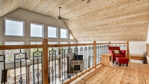 Eine Holzterrasse mit einem roten Stuhl, einem Deckenventilator und einem Geländer mit schmiedeeisernen Verzierungen.