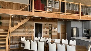 Ein geräumiger Wohnbereich im Loft-Stil mit Esstisch, weißen Stühlen, einer Treppe und einer Küche mit modernen Geräten.