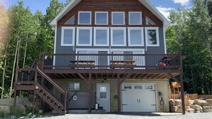 Eine zweistöckige Holzhütte mit Balkon, Garage und einer Holzterrasse.