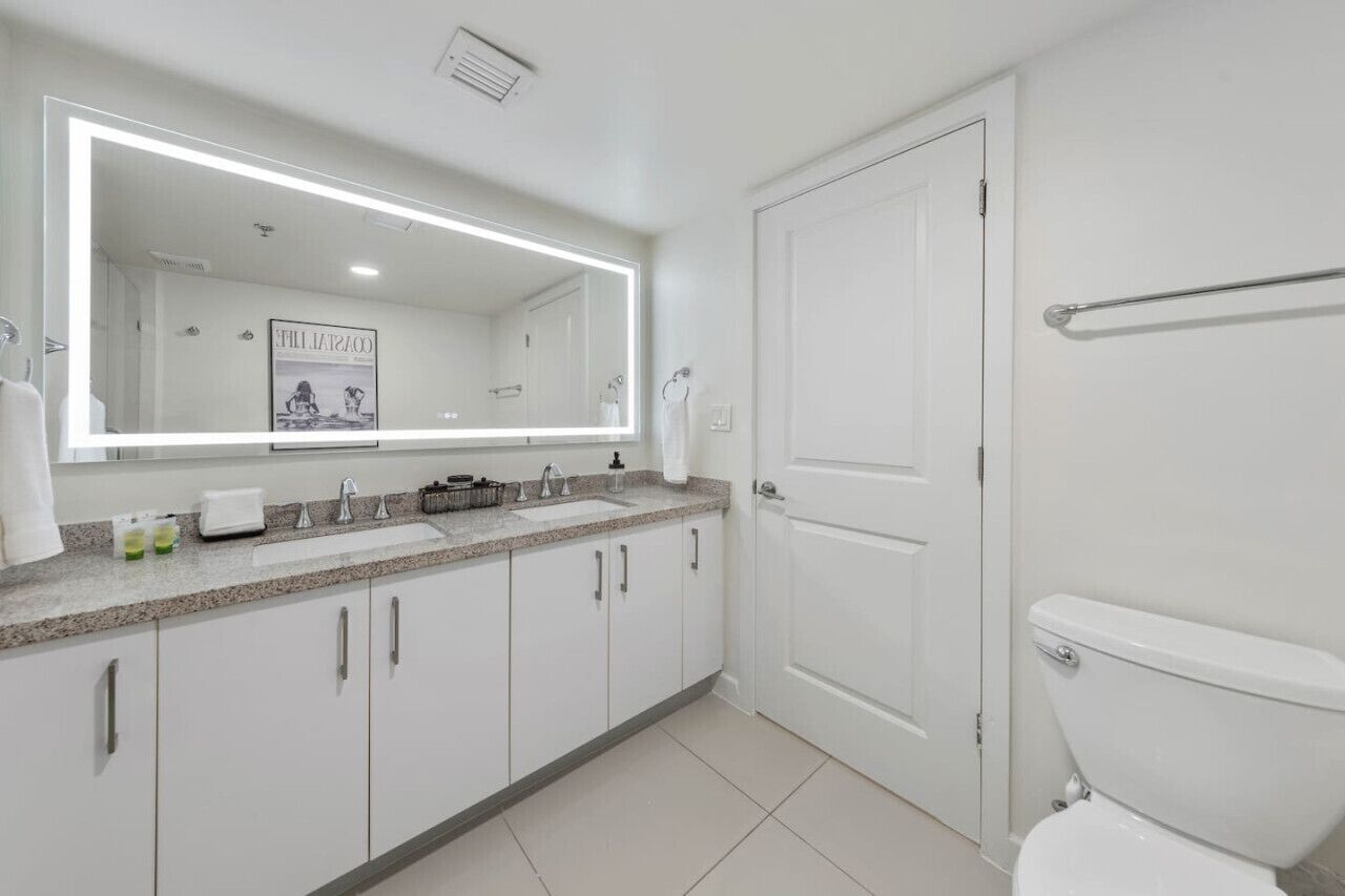 Un baño moderno con un espejo grande, dos lavamanos, un inodoro y un perchero para toallas.