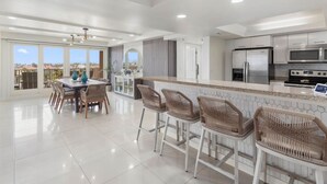 Una cocina moderna con comedor, que cuenta con una isla grande con taburetes de bar, electrodomésticos de acero inoxidable y vistas a la ciudad.