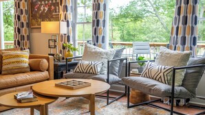 Een moderne woonkamer met een bank, fauteuils, een salontafel en uitzicht op groen.