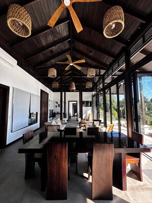 A spacious dining area with a long wooden table, multiple chairs, and woven hanging lights.