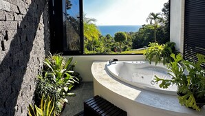 Um banheiro moderno ao ar livre, com hidromassagem, plantas em vasos e vista para o oceano.
